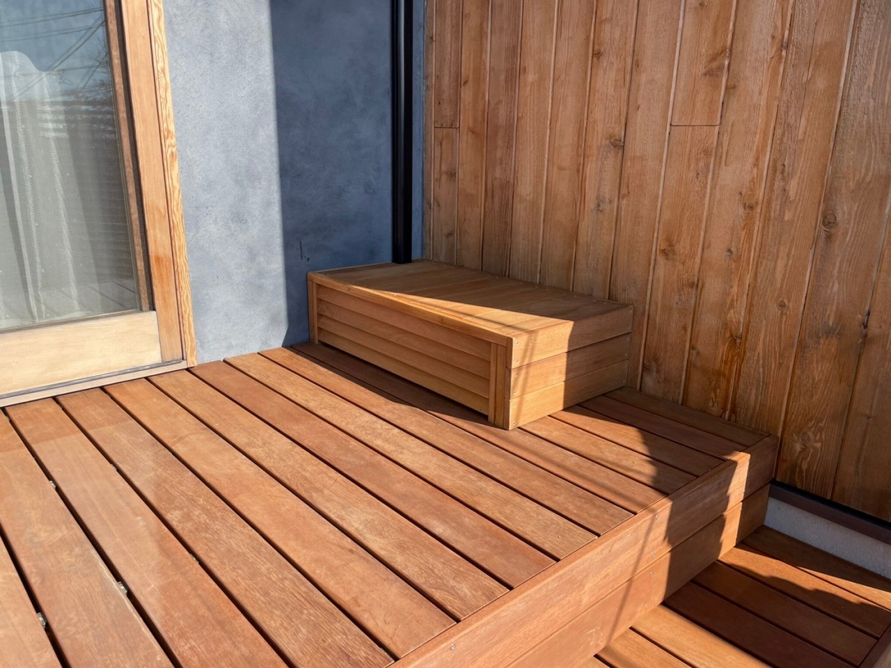 ウッドデッキの階段横に室外機カバー兼ベンチが差し込まれている画像
